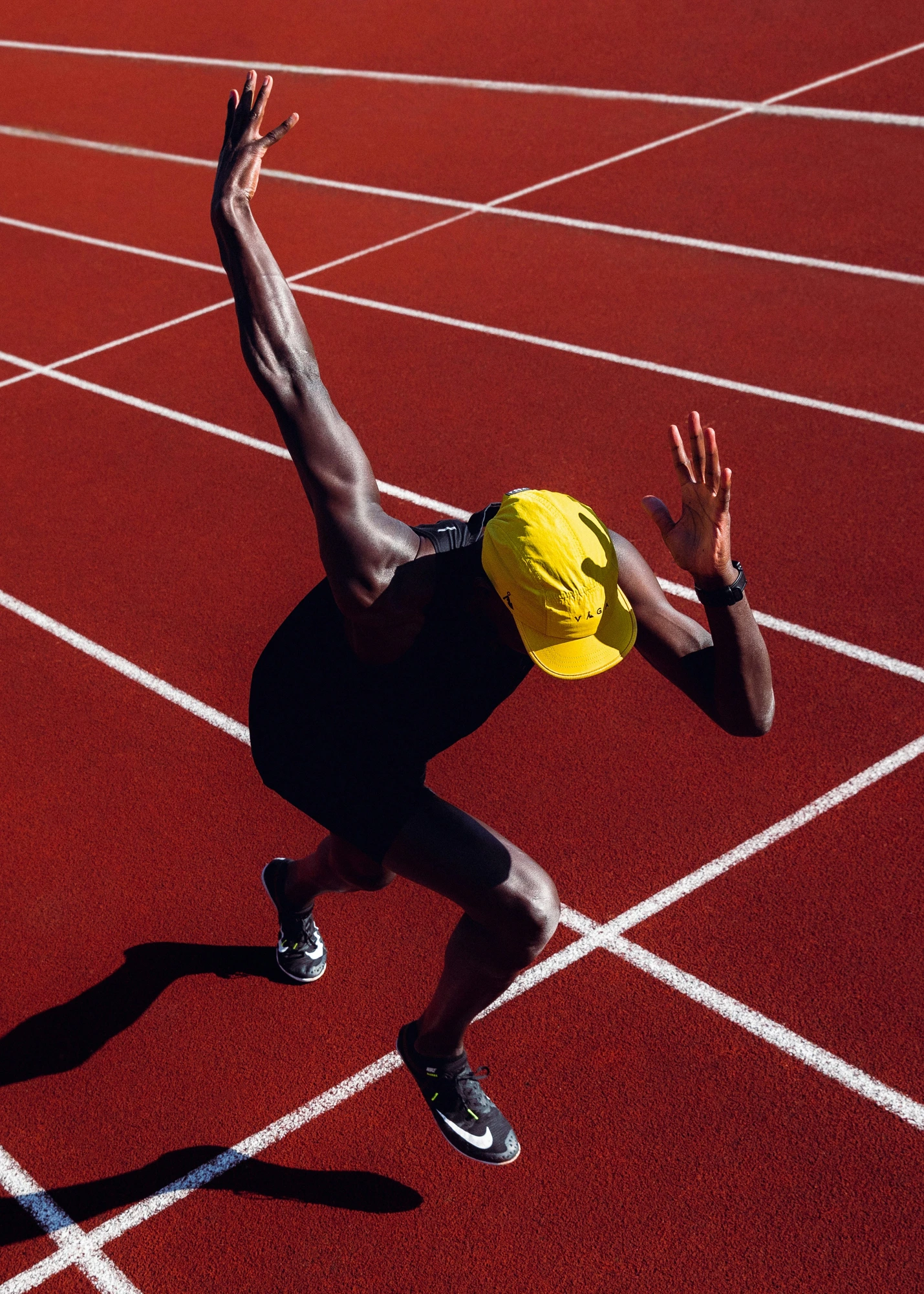 Sprinter in yellow cap seen from above on red track