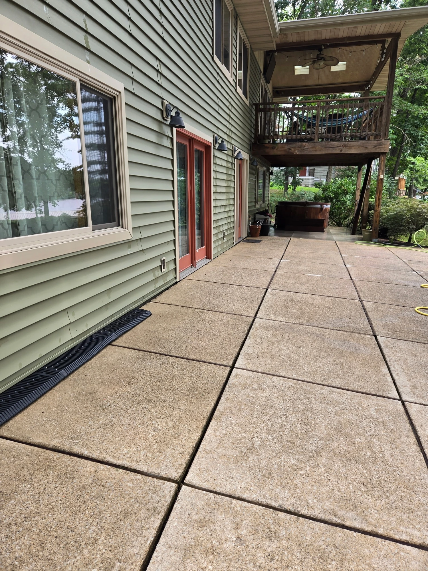 Cleaned concrete patio behind a home with green siding and hot tub