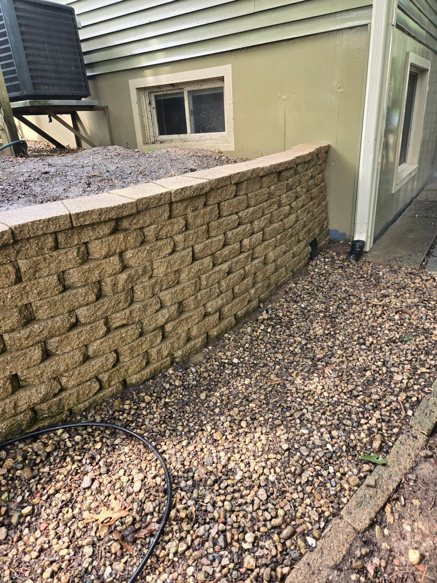 Freshly built tan interlocking-block retaining wall along a house foundation